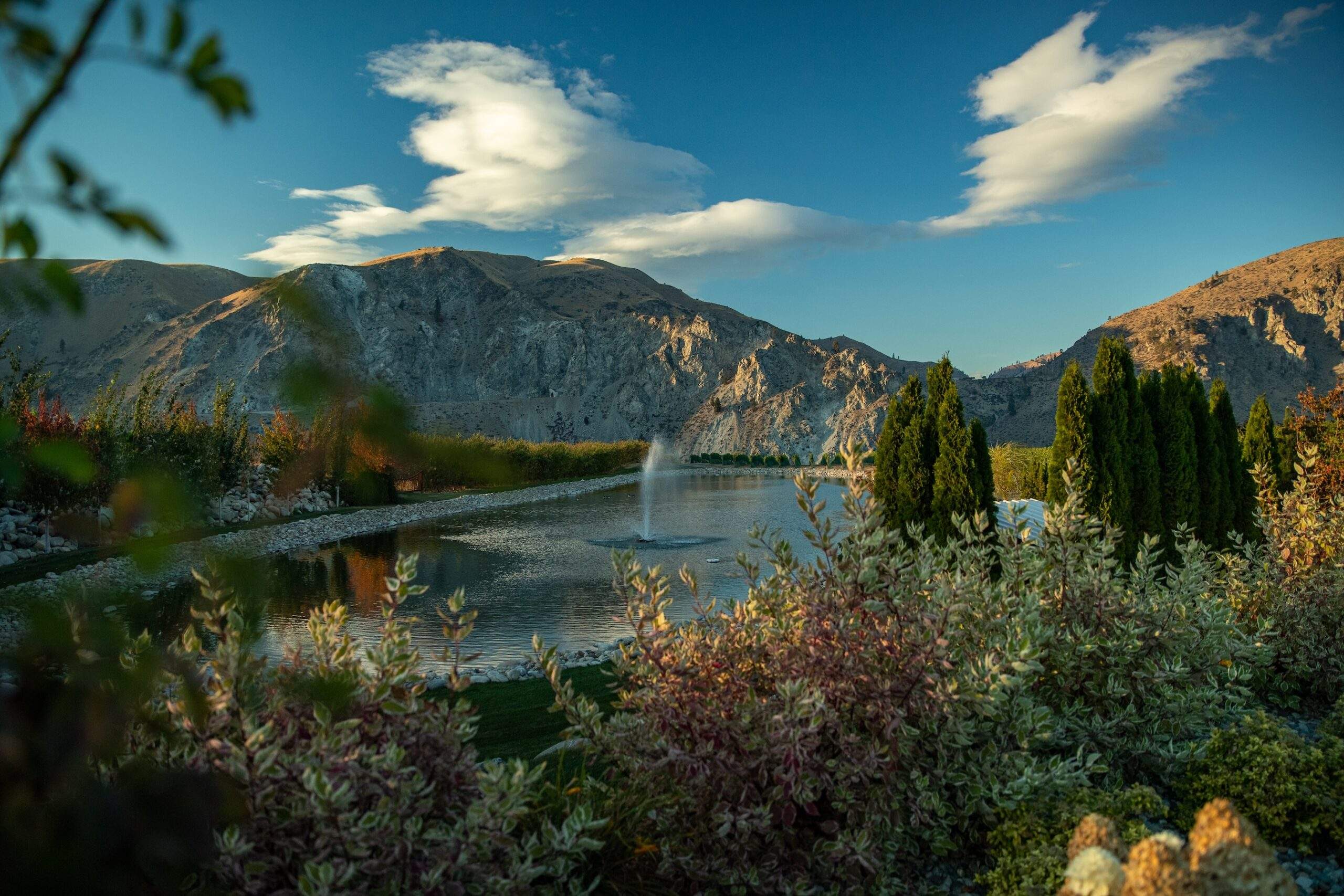 Fountain, pond, mountains, trees in evening light.
