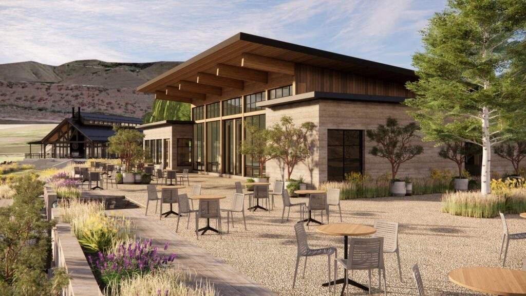 Modern building with large windows and wooden roof, surrounded by outdoor seating, plants, and trees, with hills and another structure visible in the background.