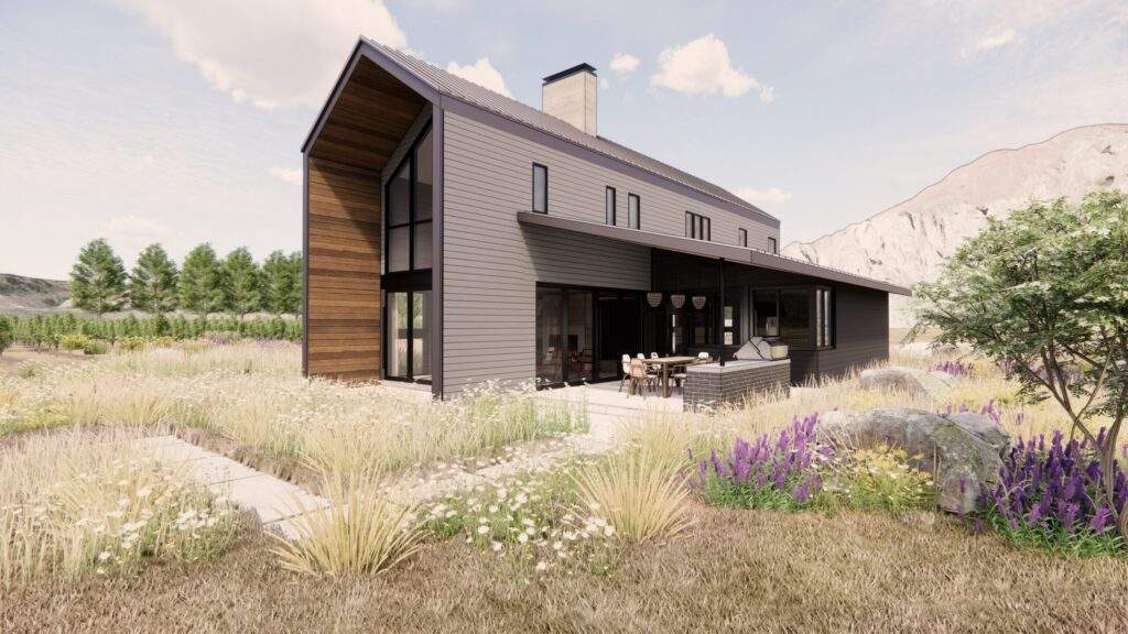 Modern two-story house with dark exterior siding, large windows, and outdoor seating area, set in a landscaped yard with grasses, wildflowers, and distant mountains near Lake Chelan with beautiful vineyard views.