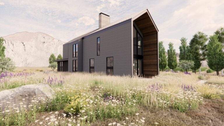 Modern two-story house with dark exterior siding, large windows, and sloped roof set in a grassy field with wildflowers and trees, offering vineyard views near Lake Chelan, with mountains in the background.