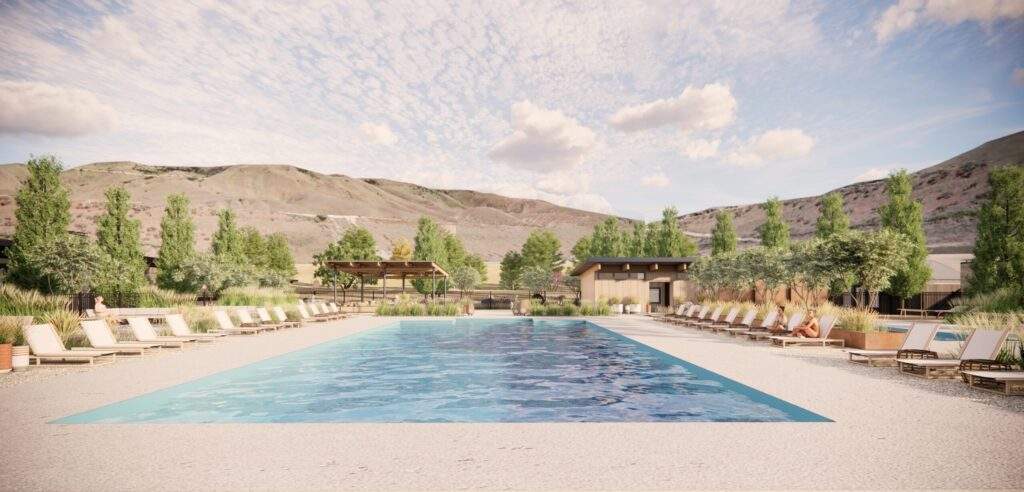 Outdoor swimming pool with lounge chairs on both sides, surrounded by trees and grassy landscaping at Rocky Pond Estate, with hills and a cloudy sky in the background near Lake Chelan in North Central Washington.