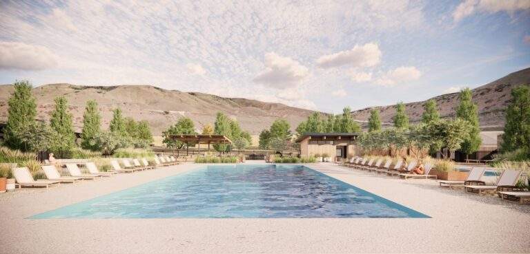 Outdoor swimming pool with lounge chairs on both sides, surrounded by trees and grassy landscaping at Rocky Pond Estate, with hills and a cloudy sky in the background near Lake Chelan in North Central Washington.