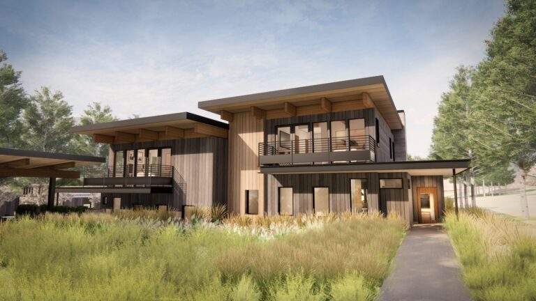 Modern two-story house with wooden siding, large windows, balconies, and a flat roof, surrounded by tall grass and trees under a partly cloudy sky, offers stunning vineyard views in the heart of North Central Washington’s Rocky Pond Estate.